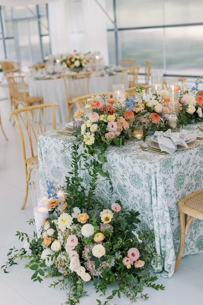 Elegant wedding reception table with green patterned linens, lush pastel floral arrangements, and candlelight inside a glass greenhouse venue at Eagle Oak Ranch.