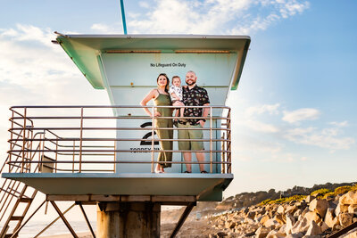 Family photographer, a family of 3 stand on a lifeguard tower smiling