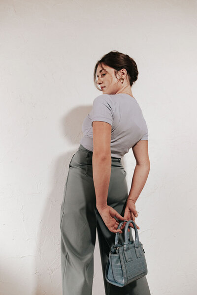 editorial style image of a woman in blue monochrome outfit holding a blue leather purse behind her back with white background