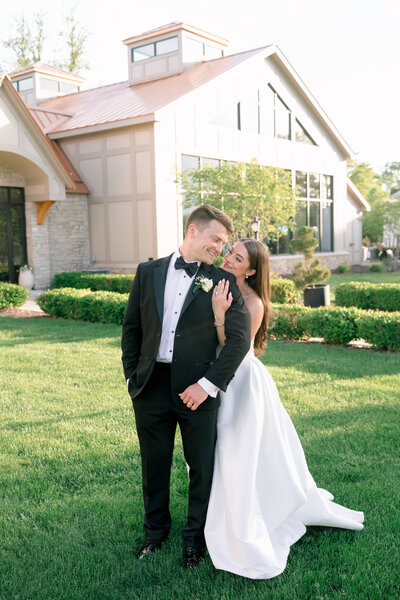 A bride and groom look at each other adoringly outside during golden hour on a green lawn in front of a manor in Michigan.