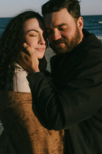 Couple embracing while the golden sun warms their skin on a cold spring evening in Newport, Rhode Island, documented by Andrea-Marie Photography