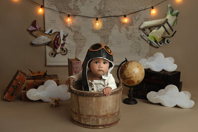 The toddler Thiago dressed up as a vintage aviator and plays in a wooden bucket