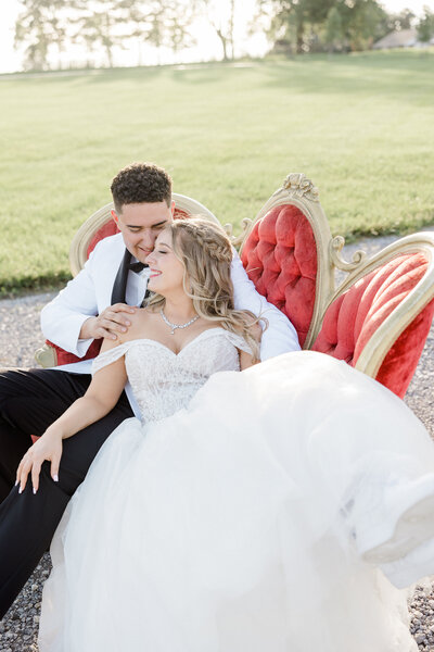 bride and groom sitting on red vintage couch photographed by Kaitlin Mendoza Photography, a wedding photographer in Indianapolis