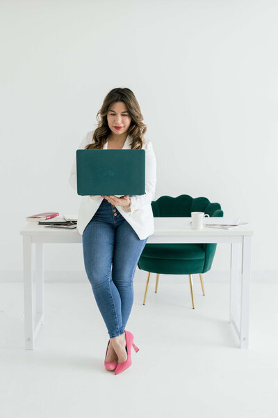 Nickie Kehoe leaning against a desk and working on a laptop