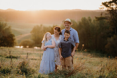 A family standing in a field of long grass in Auckland, being photographed at sunset by Auckland Photographer Tashina Narelle Photo + Video