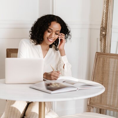Jessica wearing a white blazer, smiling as she writes in her planner