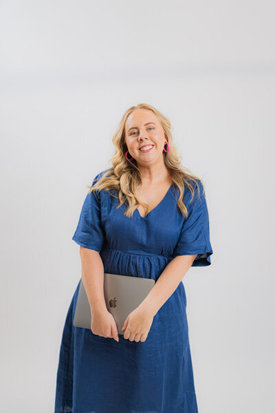 Amy Hart holding laptop wearing a blue dress