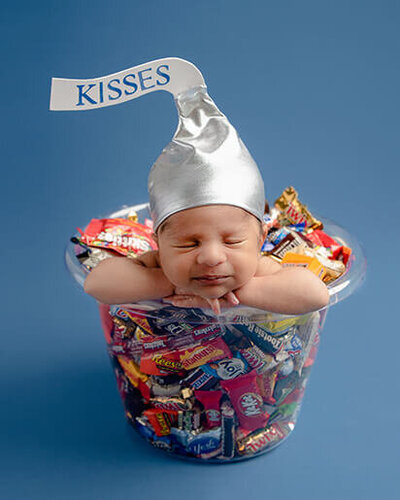The baby is wearing a candy kiss hat and he is posed in a bucket of candy.