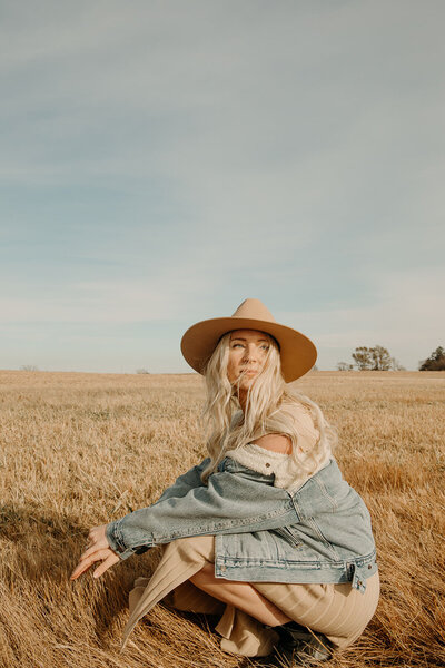 woman in hat kneels in field