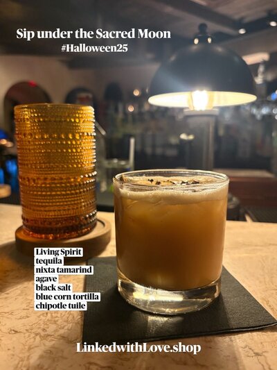 A moody autumn cocktail at dLeña in Washington, DC, featuring the Living Spirit - a tequila drink infused with ancho reyes, nixta tamarind, agave, black salt, and a chipotle tulie garnish. Warm candlelight and modern bar ambiance evoke a luxe, fall night aesthetic.
