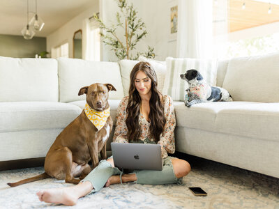 Kali, the owner of Kali Photography, sitting in a living room with her dogs editing a wedding or senior session