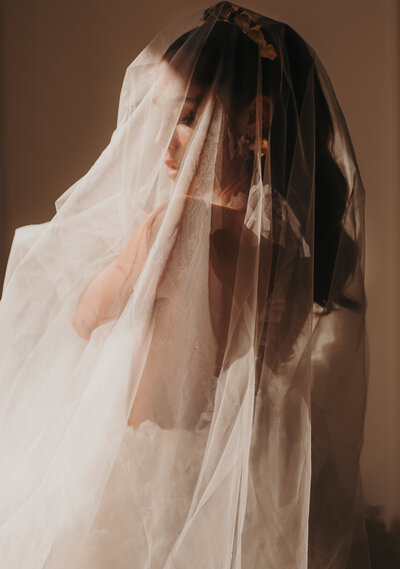 A moody photo of a bride draped in her veil, turned profile.