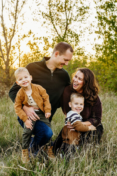 beautiful family of four snuggling and laughing together as they kneel in a field at sunset during their Green Bay Family photography session