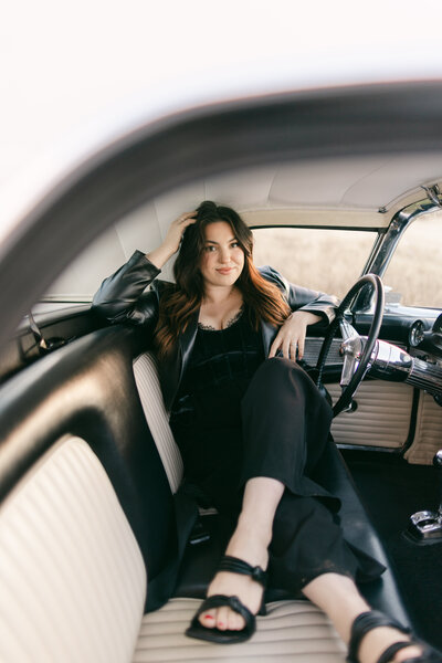 Branding portrait of a woman lounging inside a vintage black-and-white car wearing a black outfit — retro-cool branding photography in Greenville SC by Dani Lacey.