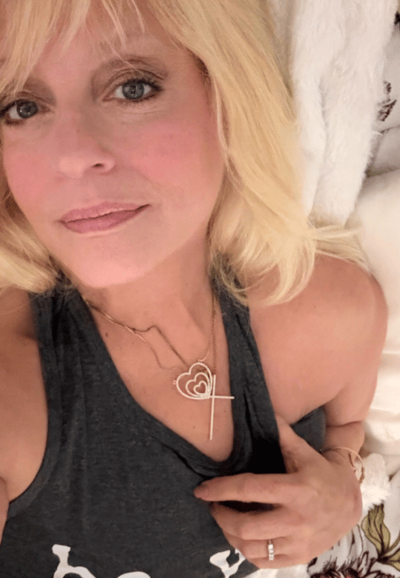 Photo of The Grammanista, a beauty, health, and fashion influencer for women over 50 showcasing a gold necklace with a heart and cross.  