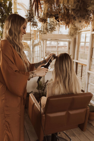 High-end hair color in North Dallas with a client. They are dressed in brown suits and her client is sitting in a hairdresser's chair.