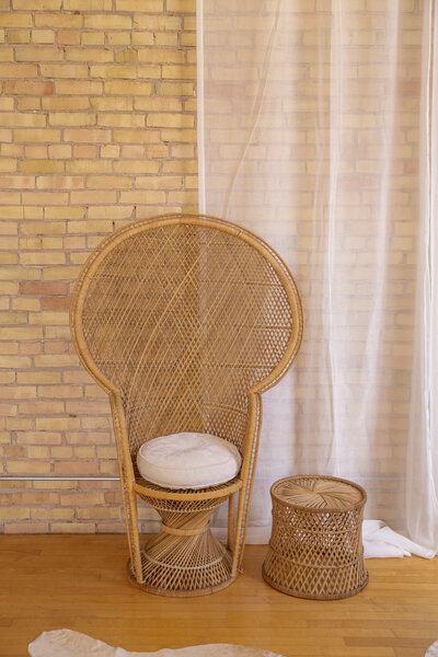 A peacock chair with white cushion next to a small round rattan end table.