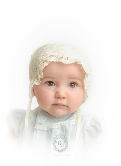 Baby girl with hazel eyes and wearing a cream lace bonnet and vintage blue dress.