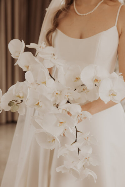 A bride holding a large bouquet of white orchids in a softly lit setting.