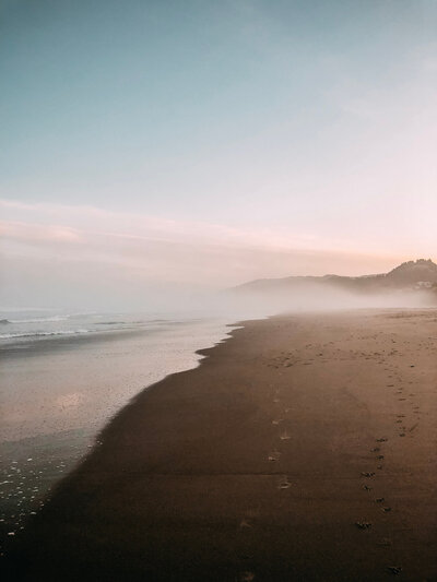 sunrise and fog over a beach with footprints