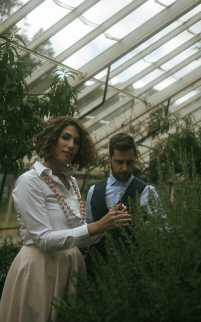 Couple enjoying a photoshoot in a lush greenhouse, surrounded by vibrant greenery and natural light, capturing intimate and romantic moments in a peaceful, nature-inspired setting