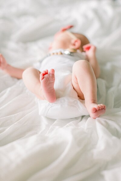 A newborn girl in a white onesie lies on a white blanket in a portrait by Katelyn Ng, Indianapolis newborn photographer.