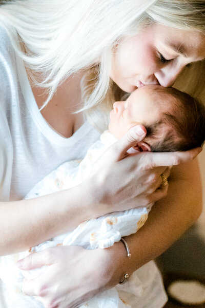Close up image of a mom kissing her newborn baby on the head