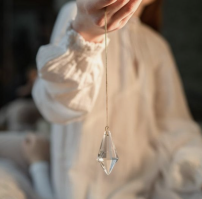 Mystic wearing a white shift holds a pendulum with clear quartz