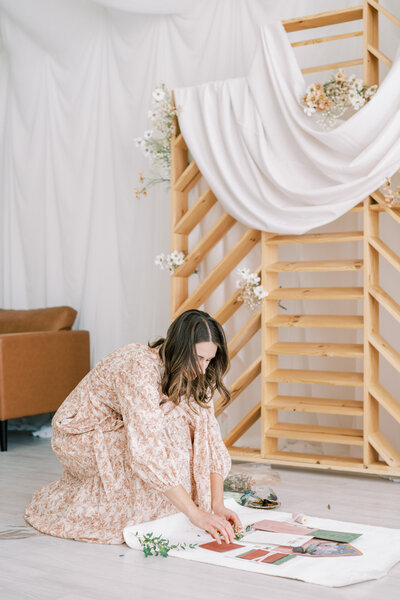 McKenna leaning over to style an invitation flatlay for a wedding suite with a shelf in the background representing full service design and calligraphy by Life in Letters.