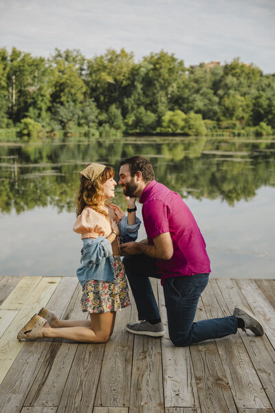 Two people kneeling down on a dock as one proposes