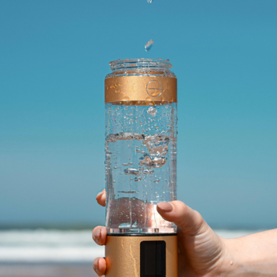 Hand holding a Lumiquench hydrogen water bottle with water droplets cascading down, showcasing advanced hydration technology.