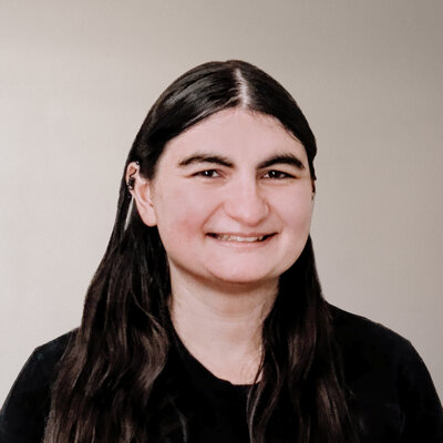 A female construction accountant focused on the construction industry, smiling warmly and wearing a black top with long, dark hair.