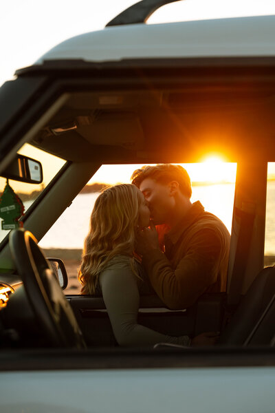 a man and woman kissing through a car window on the beach
