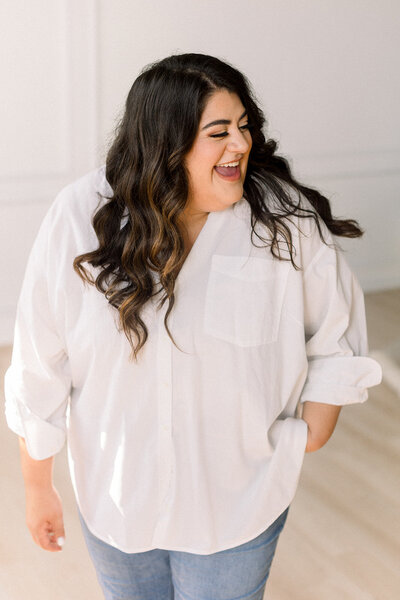 Marissa Martinez in a white top and blue jeans laughing and looking off to the side