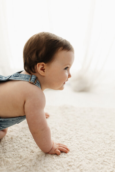 A little baby crawls along the ground  during a milestone baby photoshoot with lucy jane photography in christchurch