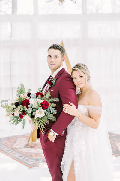 Bride embraces her groom who wears a burgundy suit