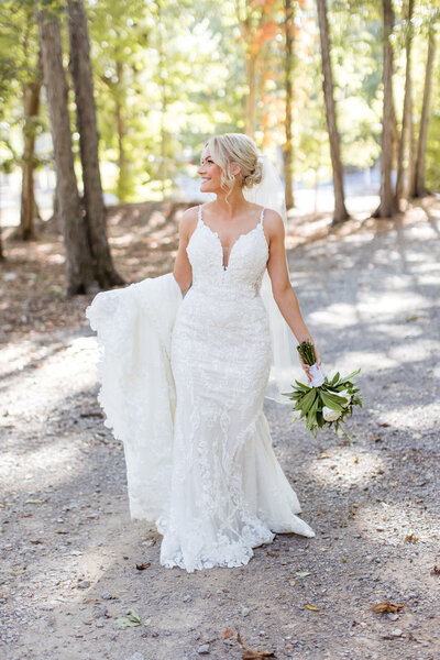 Bride holding train and walking down gravel road at Saddle Woods Farm smiling away from the camera