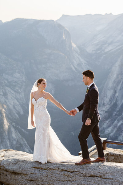 A newlywed couple with their arms around each other smiling at an overlook in Yosemite
