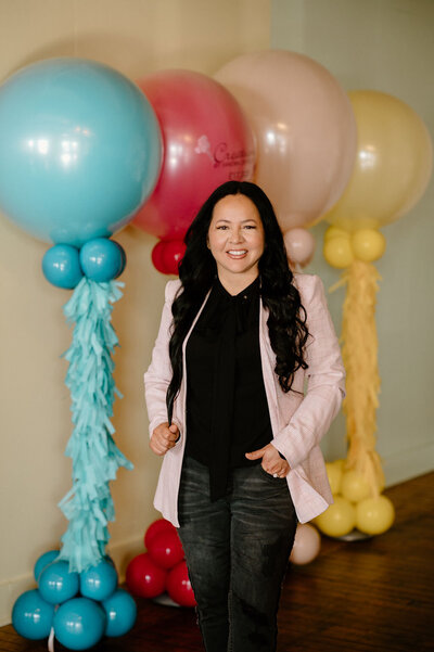 Sandra, owner of Unpoppable-FW, smiling while seated in a stylish wicker chair with black balloon decor in the background.