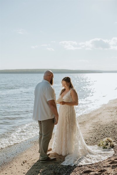 bride and groom saying vows on a beach with a lake in the background