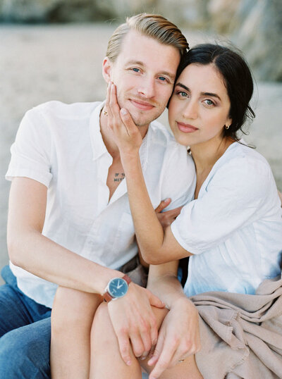 engaged couple snuggled for a photo on the beach in california