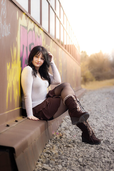 High school senior sitting on a steel graffitied wall in fall.