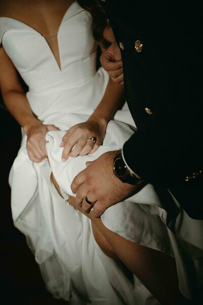 Close-up of groom's hand on bride's knee as she lifts up her dress.