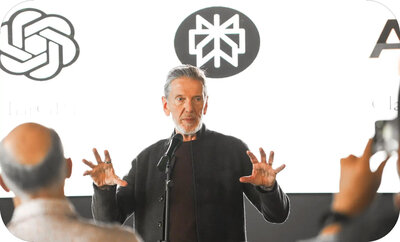 Michael Hyatt presenting on stage with a microphone, gesturing with both hands as attendees listen in the foreground. Images of AI business logos behind him