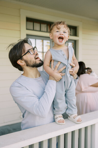 Father lifting toddler in front of a farmhouse porch | Ashley Norton Photography