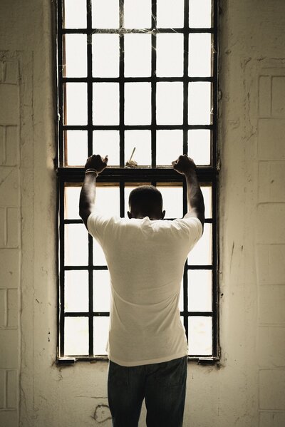 A man has his hands on a window looking down in despair in a prison cell