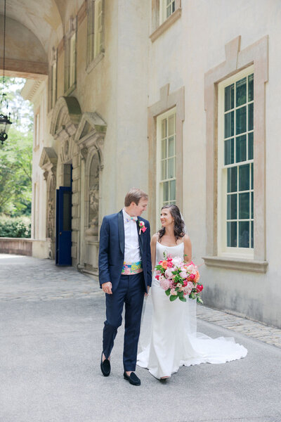 Bride holding pink bouquet looks at groom walking outside of the Swan House in Atlanta Georgia