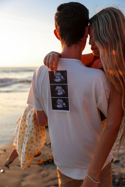 Maternity photo of pregnant woman being held by her husband by the ocean in San Diego