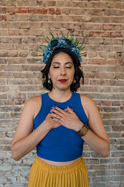 The tranquility of our art workshop creator, eyes closed, hands on chest, adorned in a yellow skirt and a pink top. The scene is completed with a touch of artistic flair – a handmade blue crown.