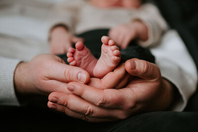 Vater hält die Füße seines neugeborenen Kindes in den Händen beim Foto Shooting mit Baby  bei Sarah Thelen